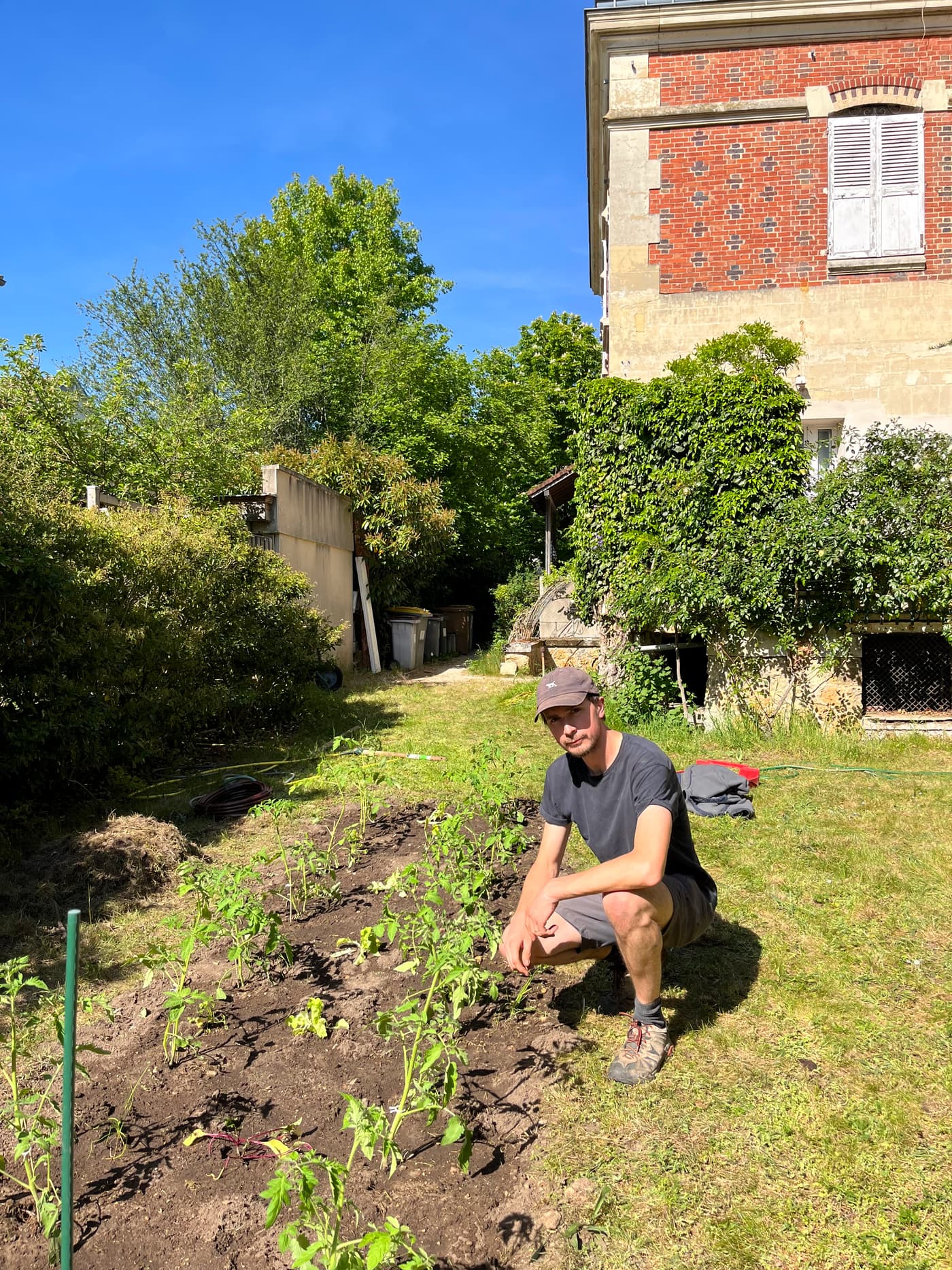 Léo accroupi en train de planter sur une butte de terre nue, lumière rasante du matin.